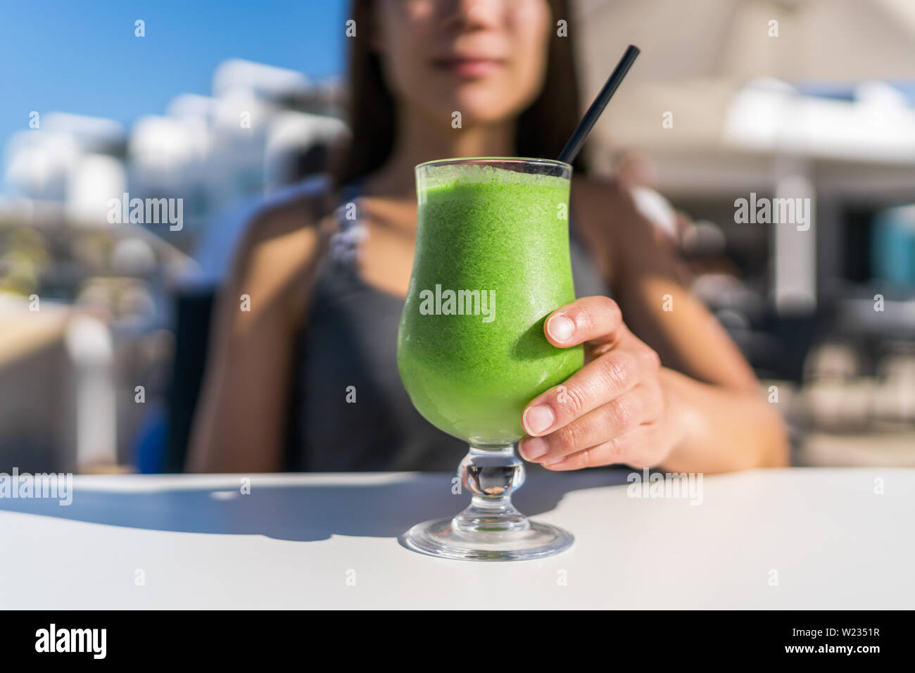 Healthy juicing lifestyle trend woman drinking green spinach juice smoothie cup at restaurant table. Unrecognizable person holding glass of fresh vegetables blend for a vegetarian diet detox cleanse . Stock Photo