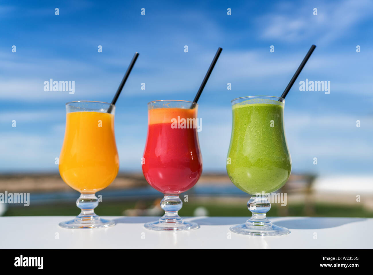 Healthy eating juicing cleanse diet trend concept - fruit and vegetable juice glasses on outdoor cafe table. Green smoothie or cold-pressed juices. Orange, beet and spinach green smoothie cups. Stock Photo