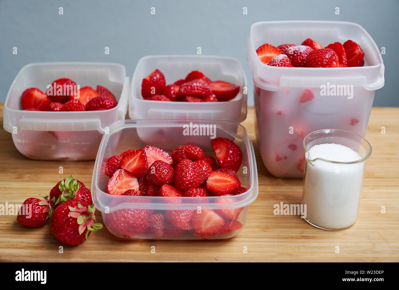 Fresh strawberries in plastic boxes ready for freezing and suger mug on wooden table Stock Photo