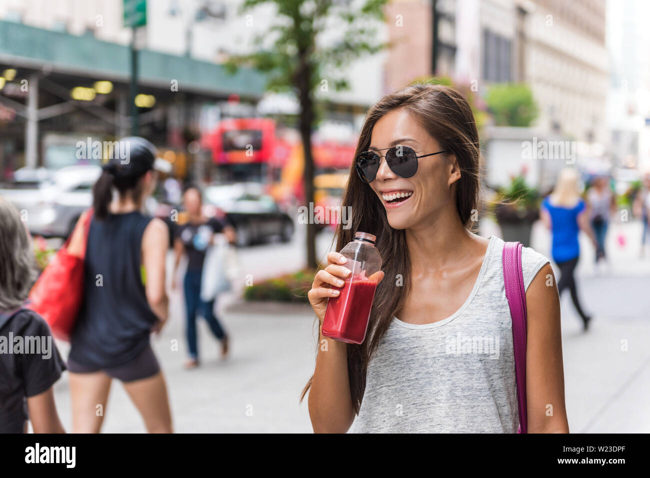 Urban city lifestyle hipster asian woman drinking healthy fruit vegetable berry juice smoothie walking on downtown street of New York city, NYC, USA. Happy young adult health diet concept. Stock Photo
