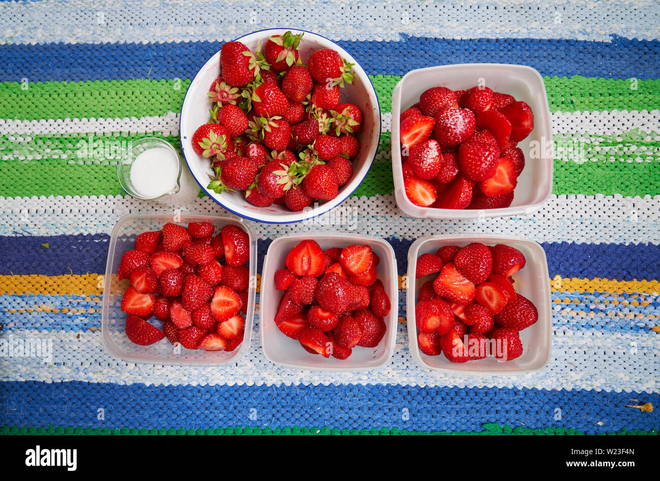 Fresh strawberries in plastic boxes ready for freezing and suger mug on colourful rag rug Stock Photo