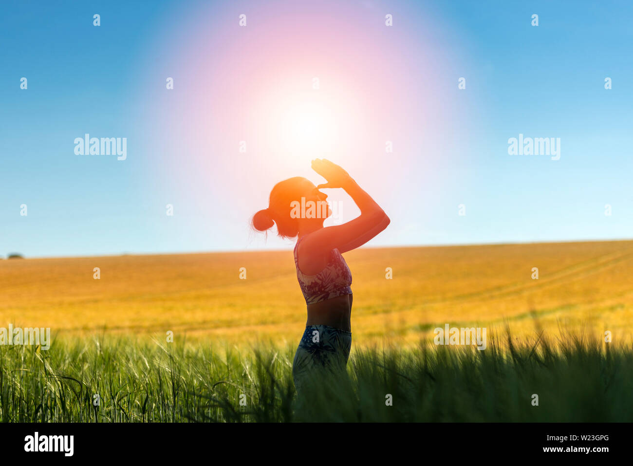 woman standing in a field meditating with sun in the sky, yoga pose. Stock Photo