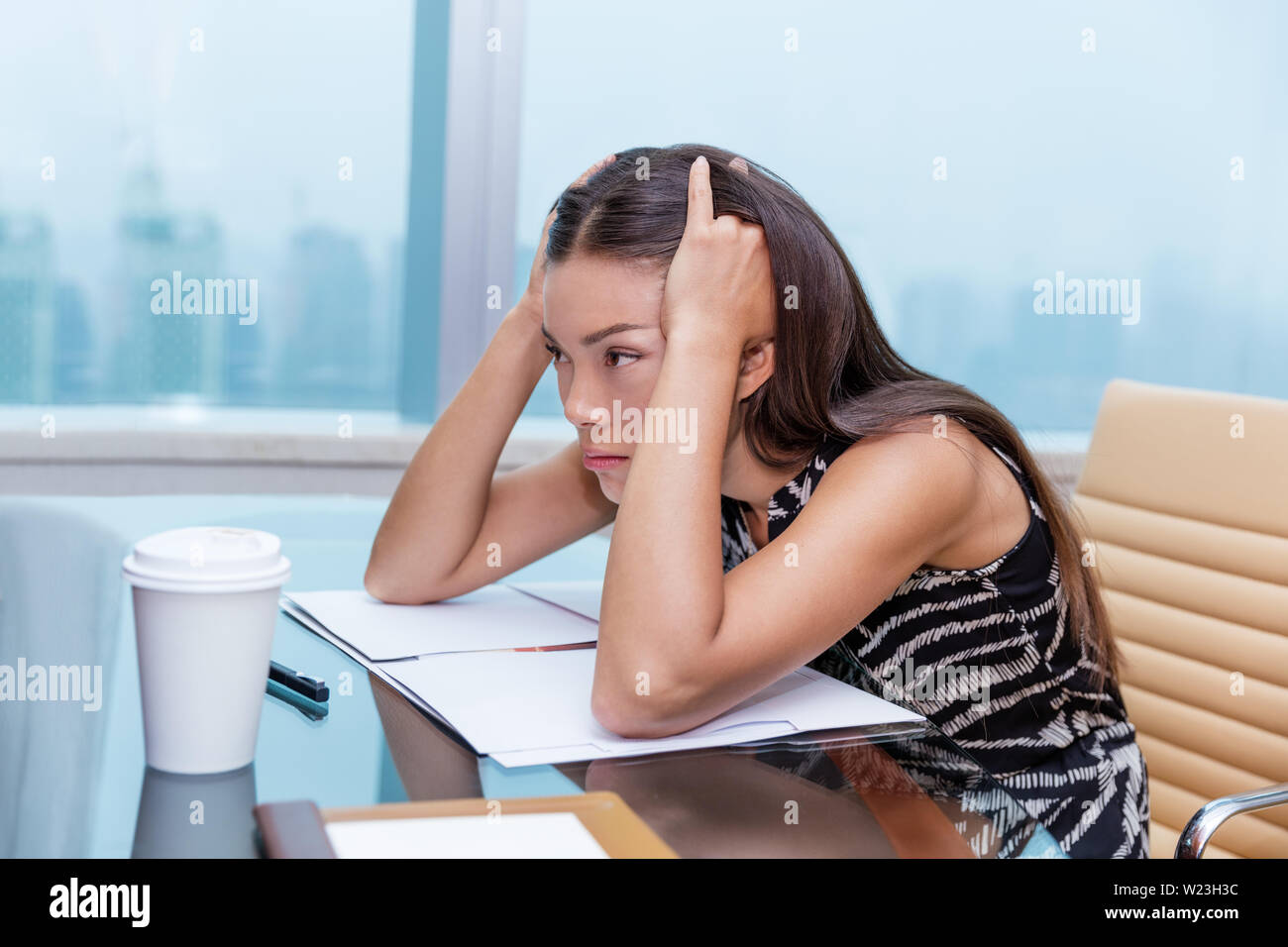 Stressed business woman at office desk stressing about work. Negative concept, headache, migraine. Tired businesswoman sitting thinking about problems and showing dissatisfaction of career. Stock Photo