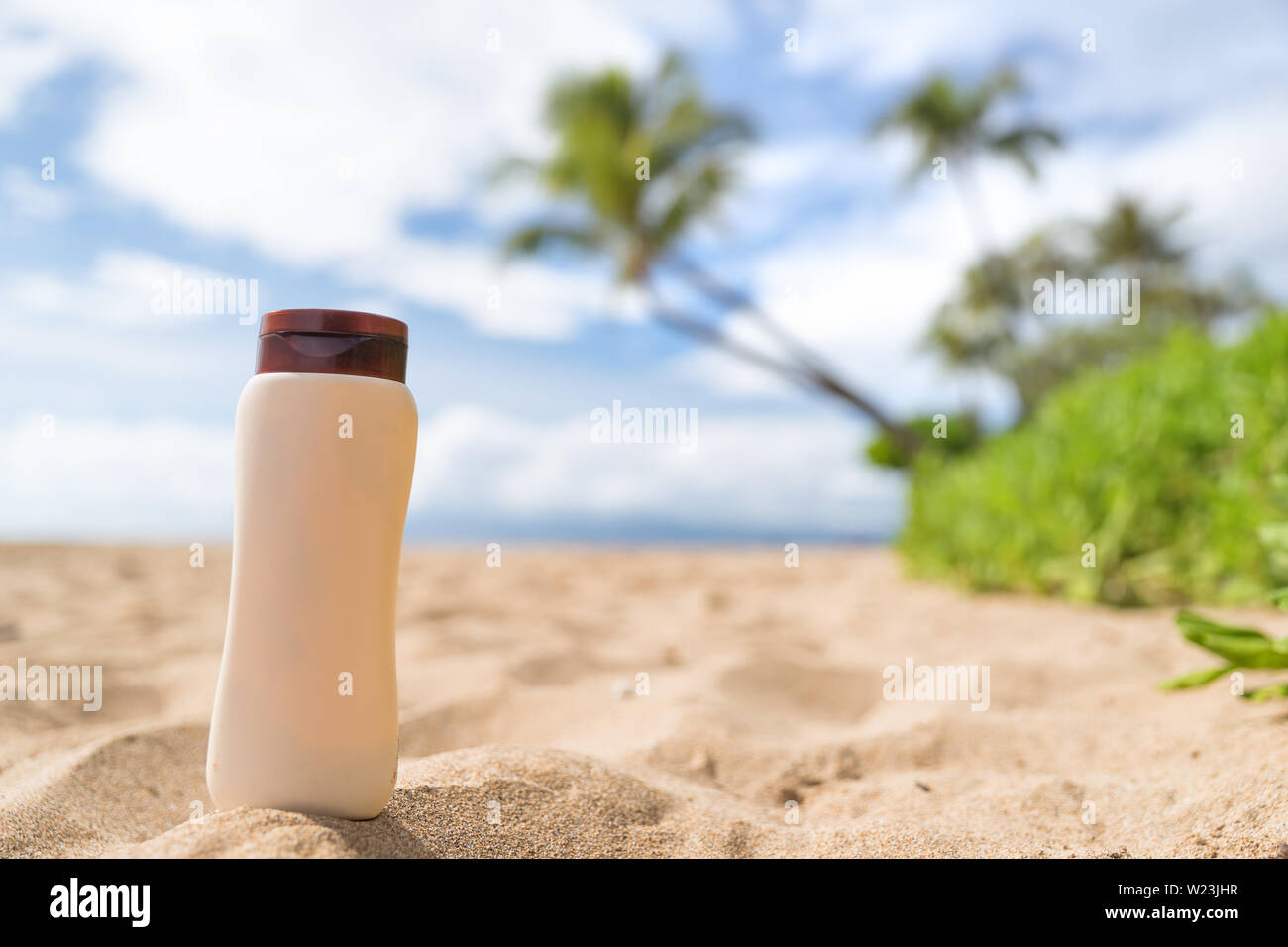 Blank sunscreen sun lotion bottle lying in golden sand on hawaii beach vacation tropical background. Sunny summer day with sunblock cream plastic container - uv protection skincare concept. Stock Photo