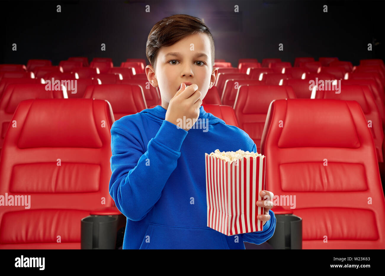 boy in blue hoodie eating popcorn at movie theater Stock Photo Alamy