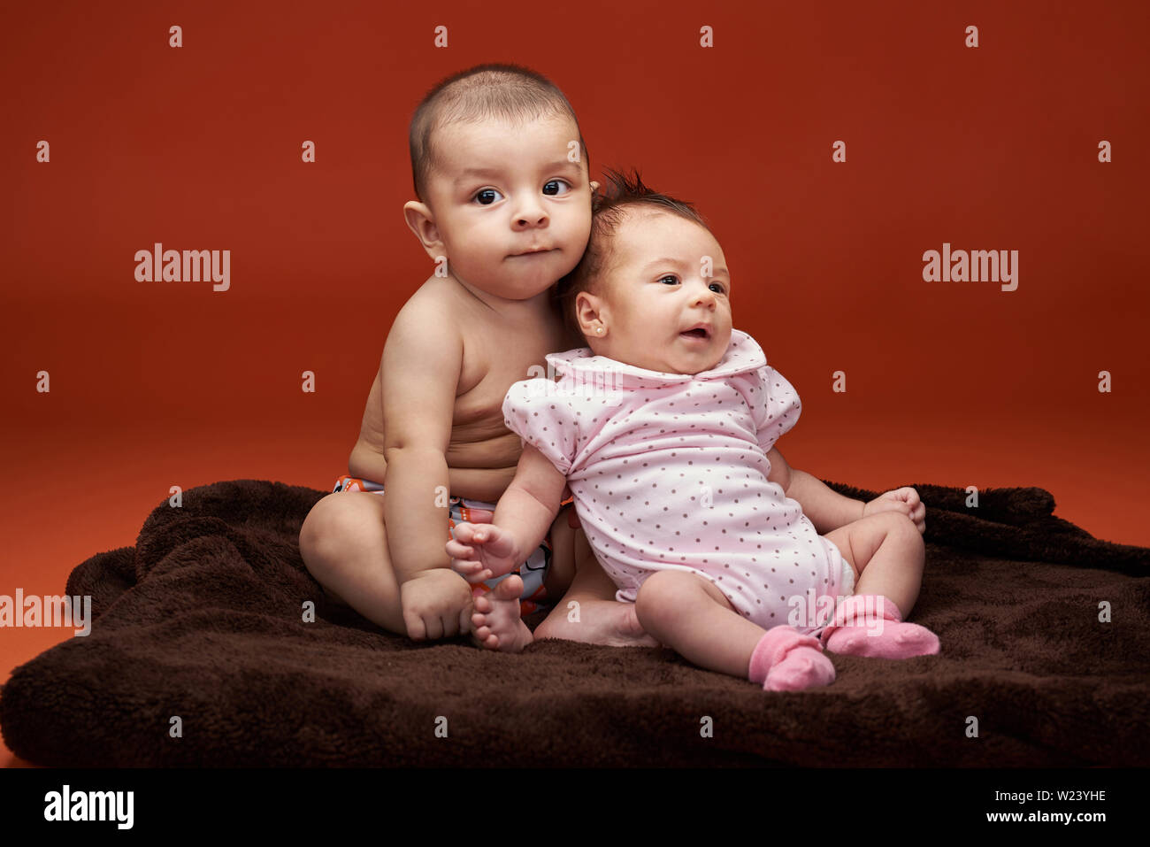 Portrait of two cute little babies sitting in orange color studio background Stock Photo
