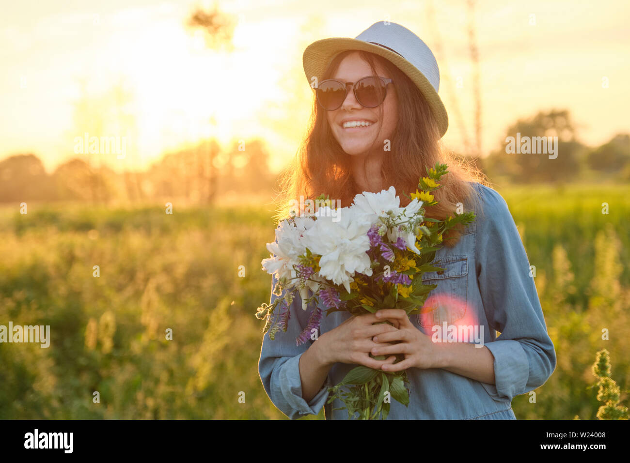 Outdoor portrait of a young girl with flowers on a meadow, golden hour ...