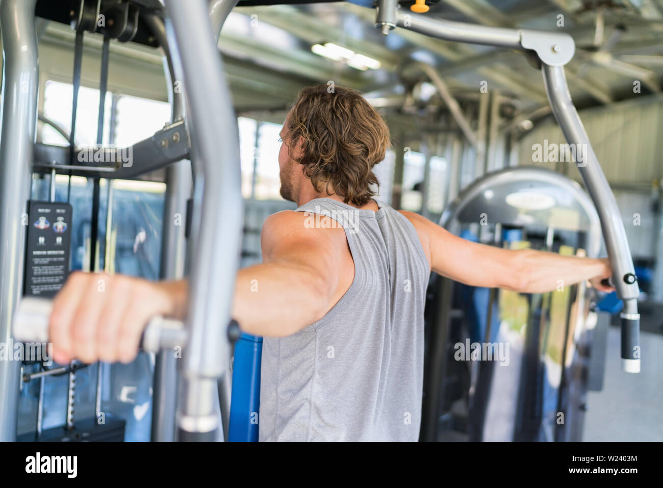 Man from behind training at fitness gym. Man doing workout on