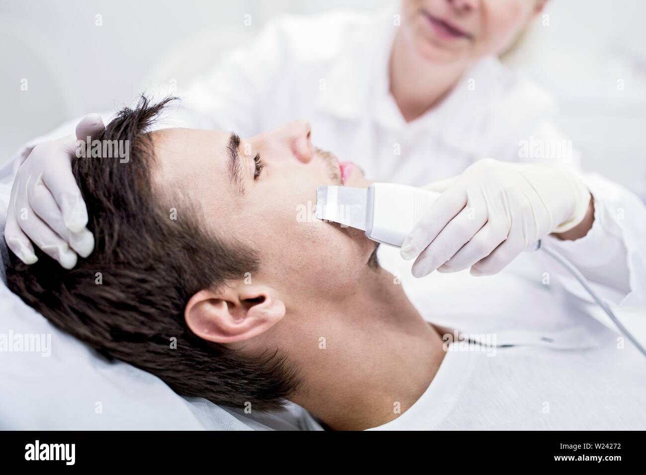 Dermatologist applying facial microdermabrasion treatment on man in clinic, close-up. The cosmetic procedure uses micro crystals to remove dead skin c Stock Photo