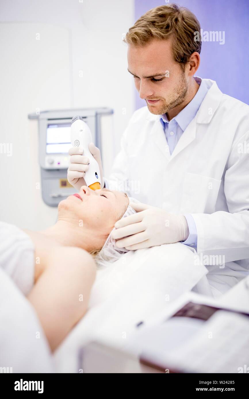 Dermatologist giving thermage treatment to mature woman's face to soften wrinkles. Stock Photo
