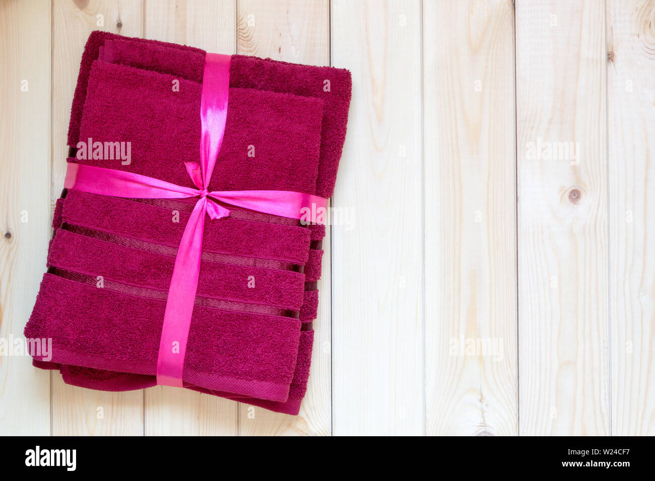 New red terry towels tied with a pink ribbon are lying on a light wooden table, like a gift. Copy space. View from above. Close-up. Body care concept. Stock Photo
