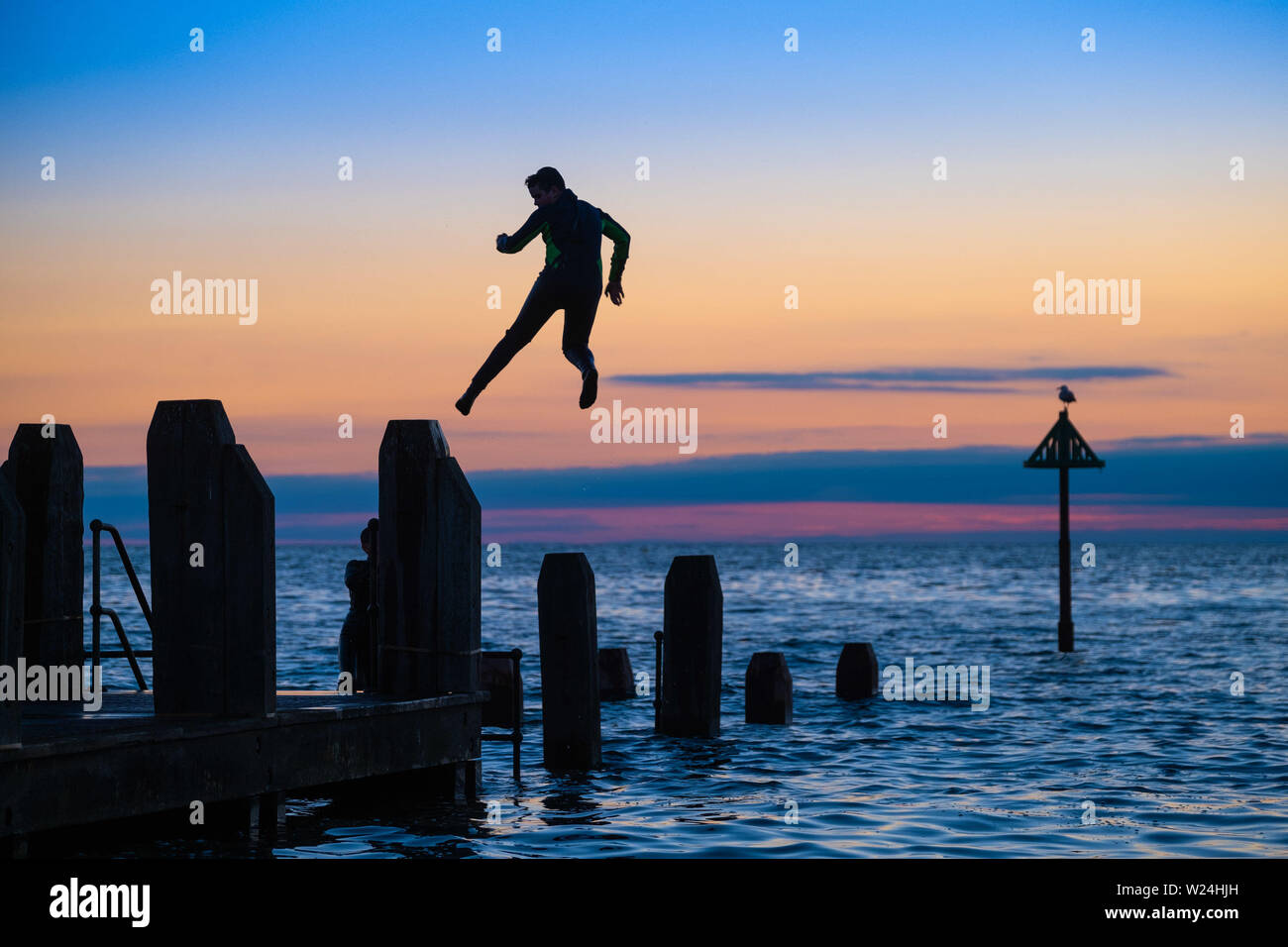 Aberystwyth Wales UK, Friday 05 July 2019  UK Weather: In the fading light at the end of a day of hot sunshine, two youngsters cool off by jumping acrobatically  into the sea off the wooden jetty in Aberystwyth on the Cardigan Bay coast, west Wales.   photo credit: Keith Morris/Alamy Live News Stock Photo