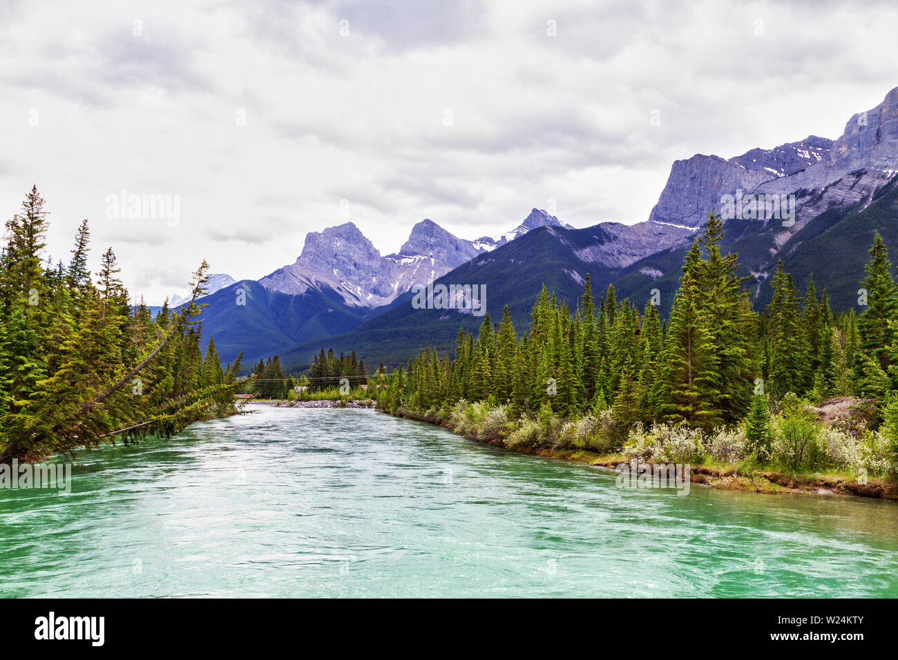 Bow River in Canmore with the Canadian Rockies mountain ranges of The Three Sisters and Ehagay Nakoda in the background. Stock Photo