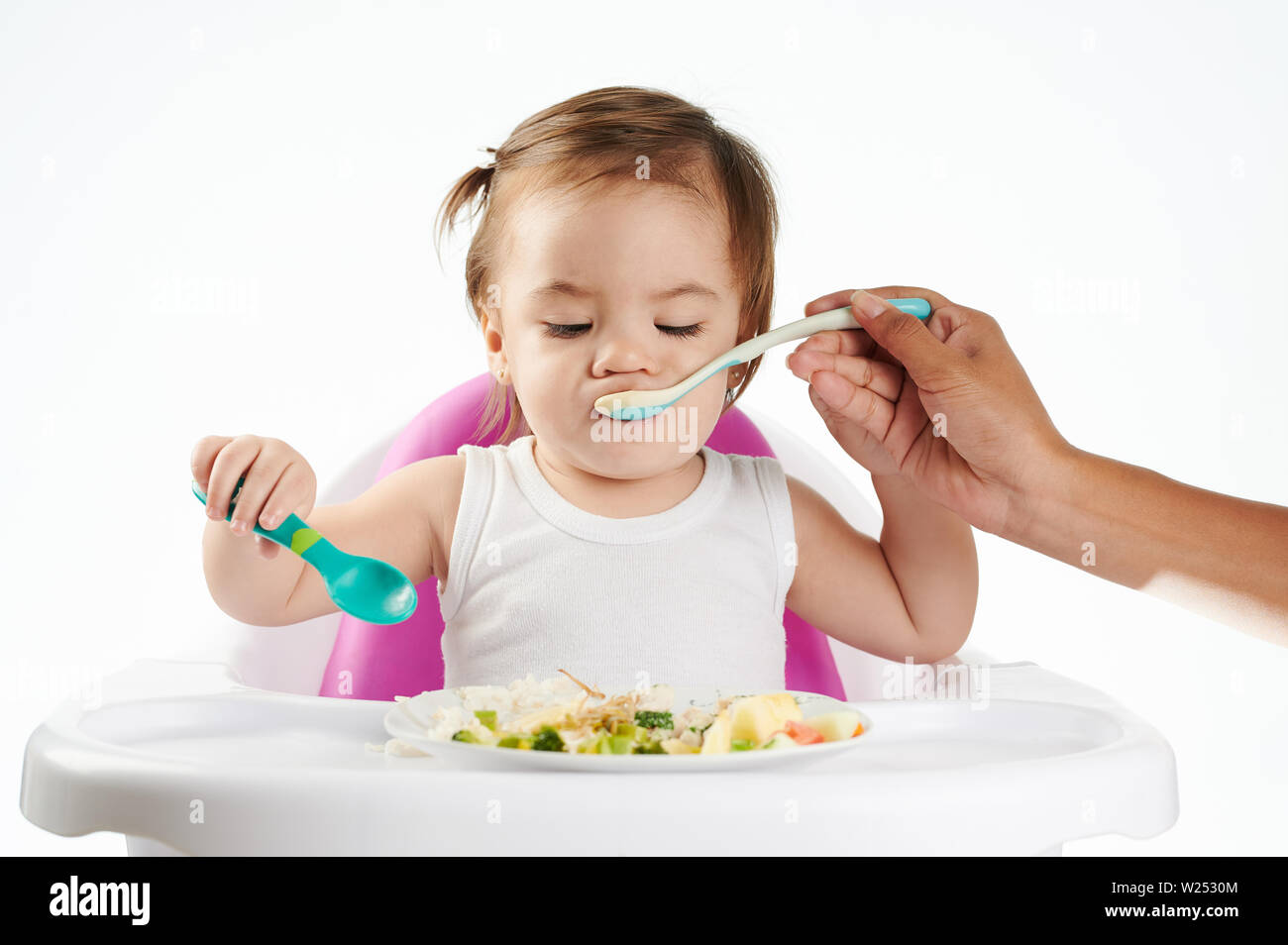 Mom feeding baby with spoon isolated on white studio background Stock Photo