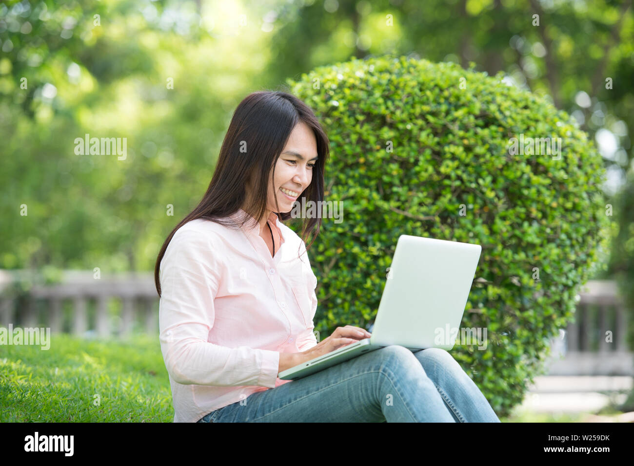 Young Asian beautiful woman with smiling face working outdoor in a public park. Working on laptop outdoors. Cropped image of female working on laptop Stock Photo