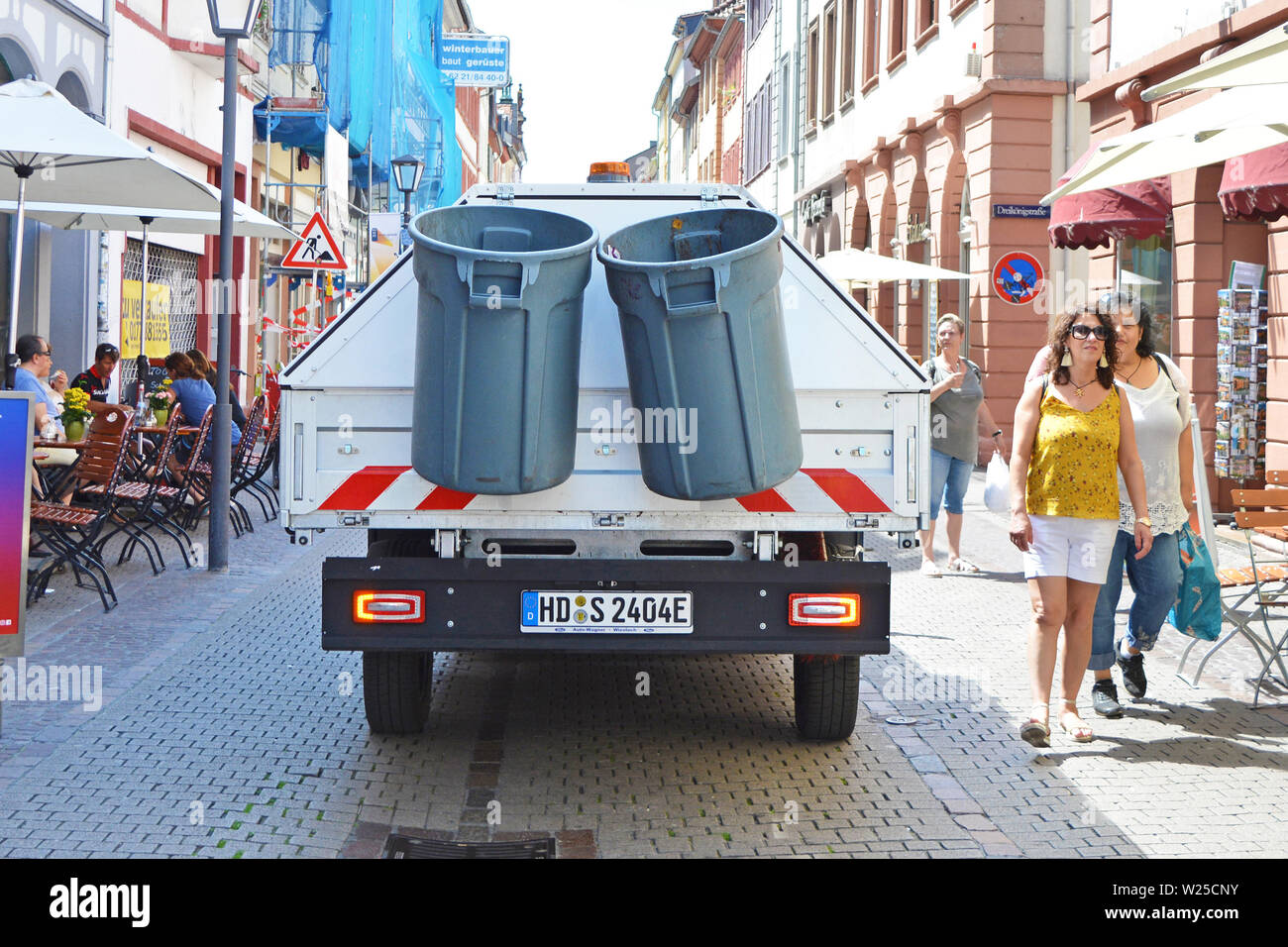 Back of small garbage collection truck driving through narrow street with people in city center of Heidelberg, Germany Stock Photo