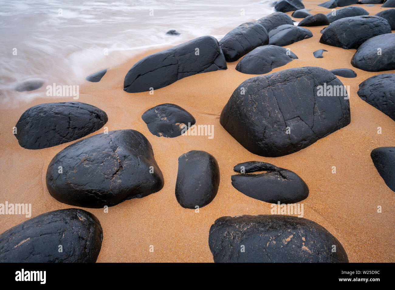 Dolerite boulders on Embleton Bay beach with the North Sea washing in, Northumberland, England Stock Photo