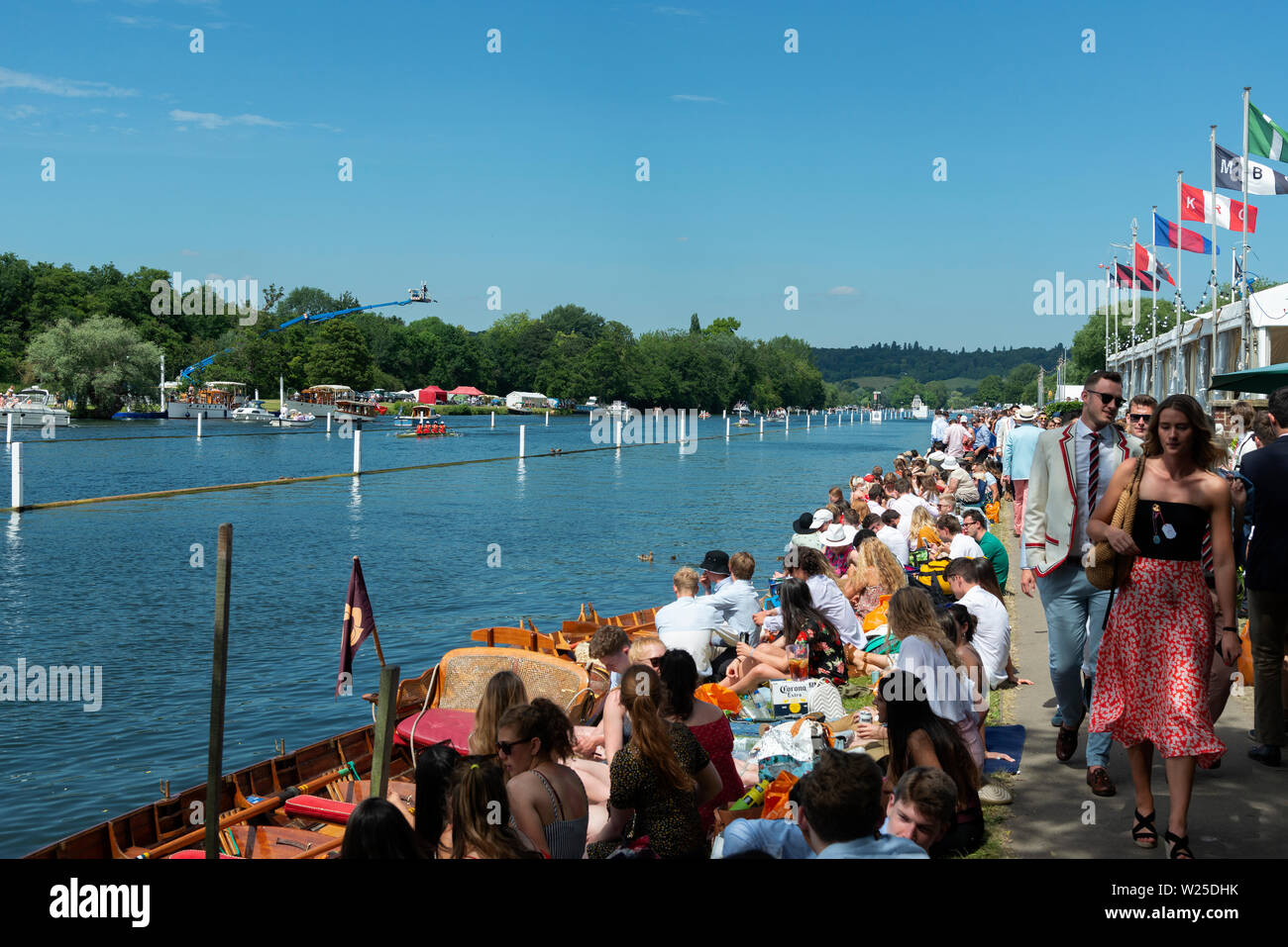 People line the banks of the River Thames during the Henley Royal Regatta to picnic and cheer on the rowing crews. Henley-on-Thames, England, UK Stock Photo