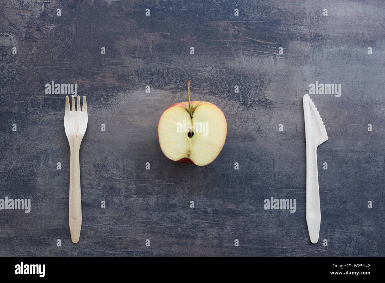 Top view of fork, knife and apple cut in half, on background of marble kitchen counter. Natural wooden cutlery. Stock Photo