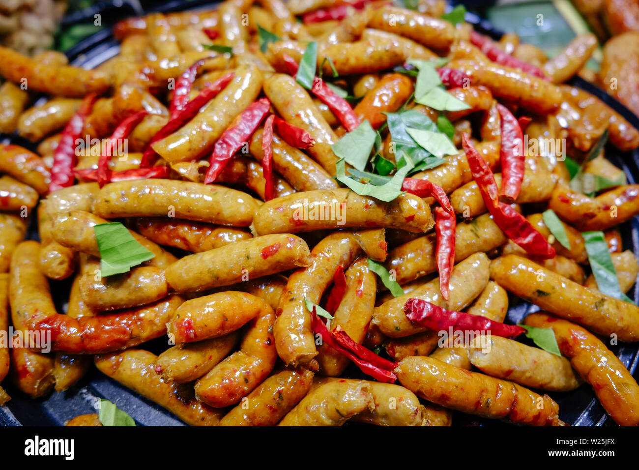Northern Thai spicy herbal sausages freshly cooked in a pan for sale in local market, Thailand. Ready to eat street food. Stock Photo
