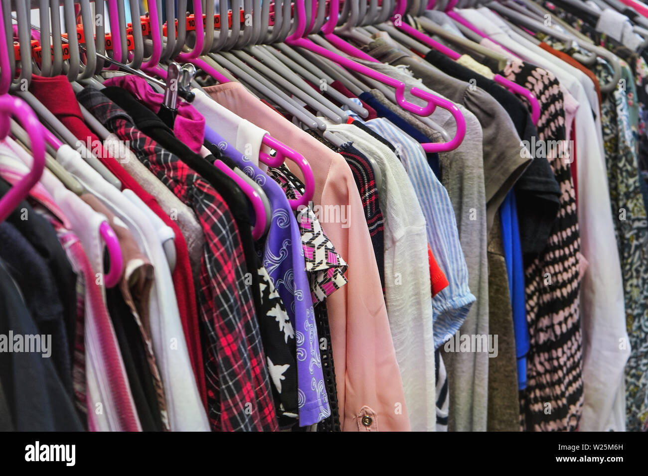 Various women clothing on mostly pink coat hangers inside charity second hand thrift shop Stock