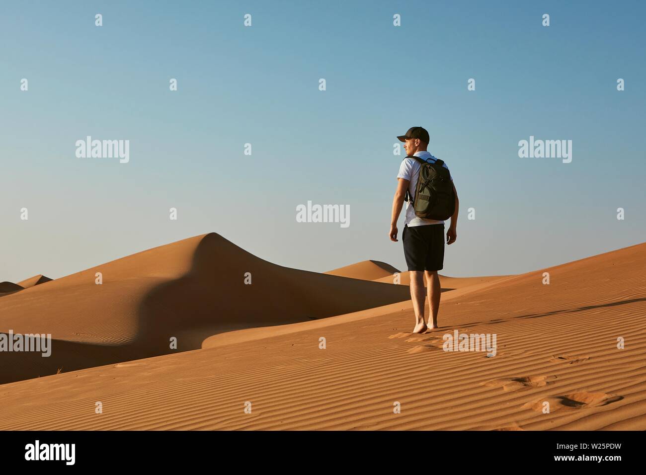 Young tourist in desert. Man with backpack walking on sand dune. Desert Wahiba Sands in Oman. Stock Photo
