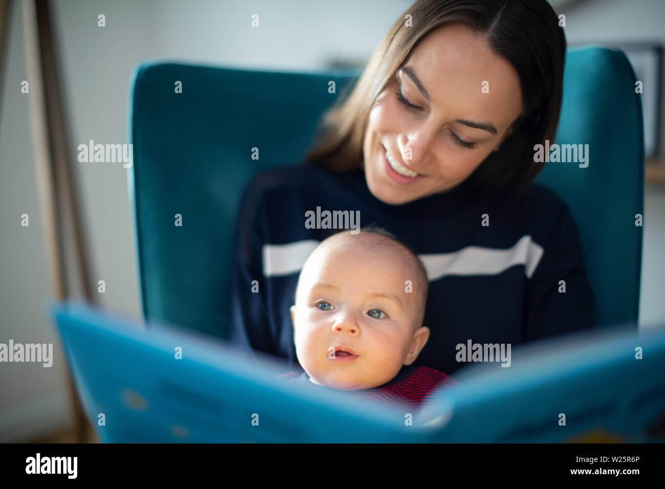 Baby Son Sitting On Mothers Lap Reading Story Book Together Stock Photo