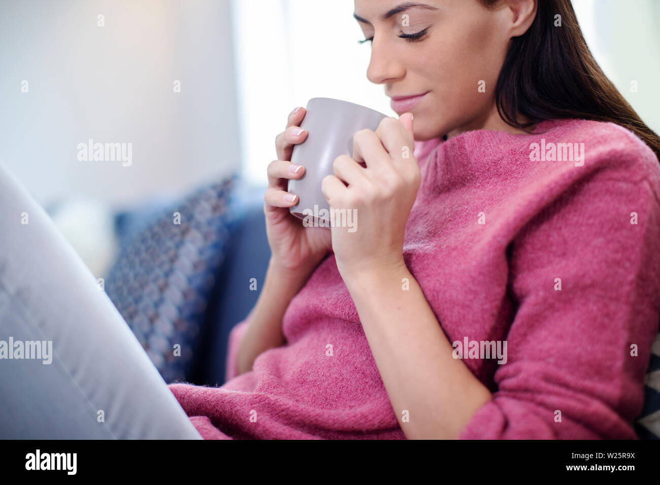 Young Woman Relaxing On Sofa With Hot Drink Stock Photo