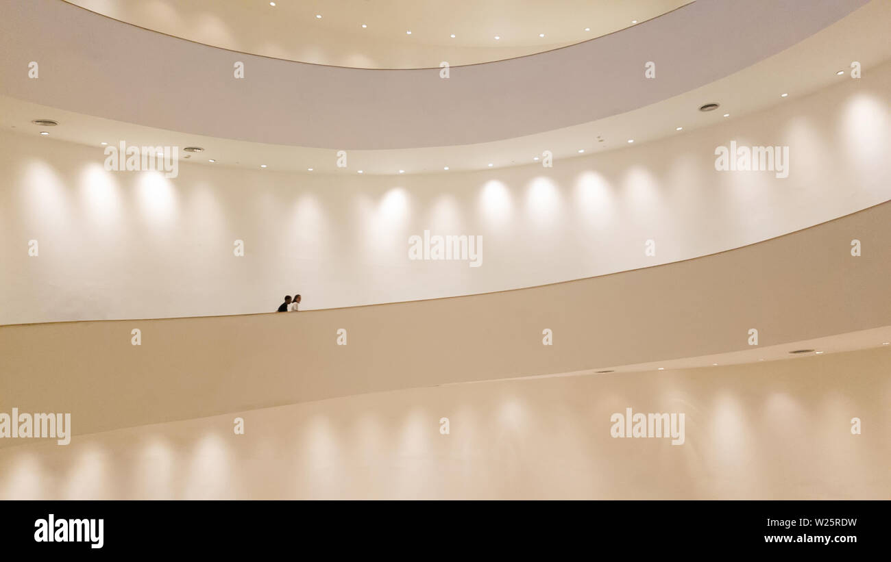 white spiral staircase with white wall with spotlight and people walking Stock Photo