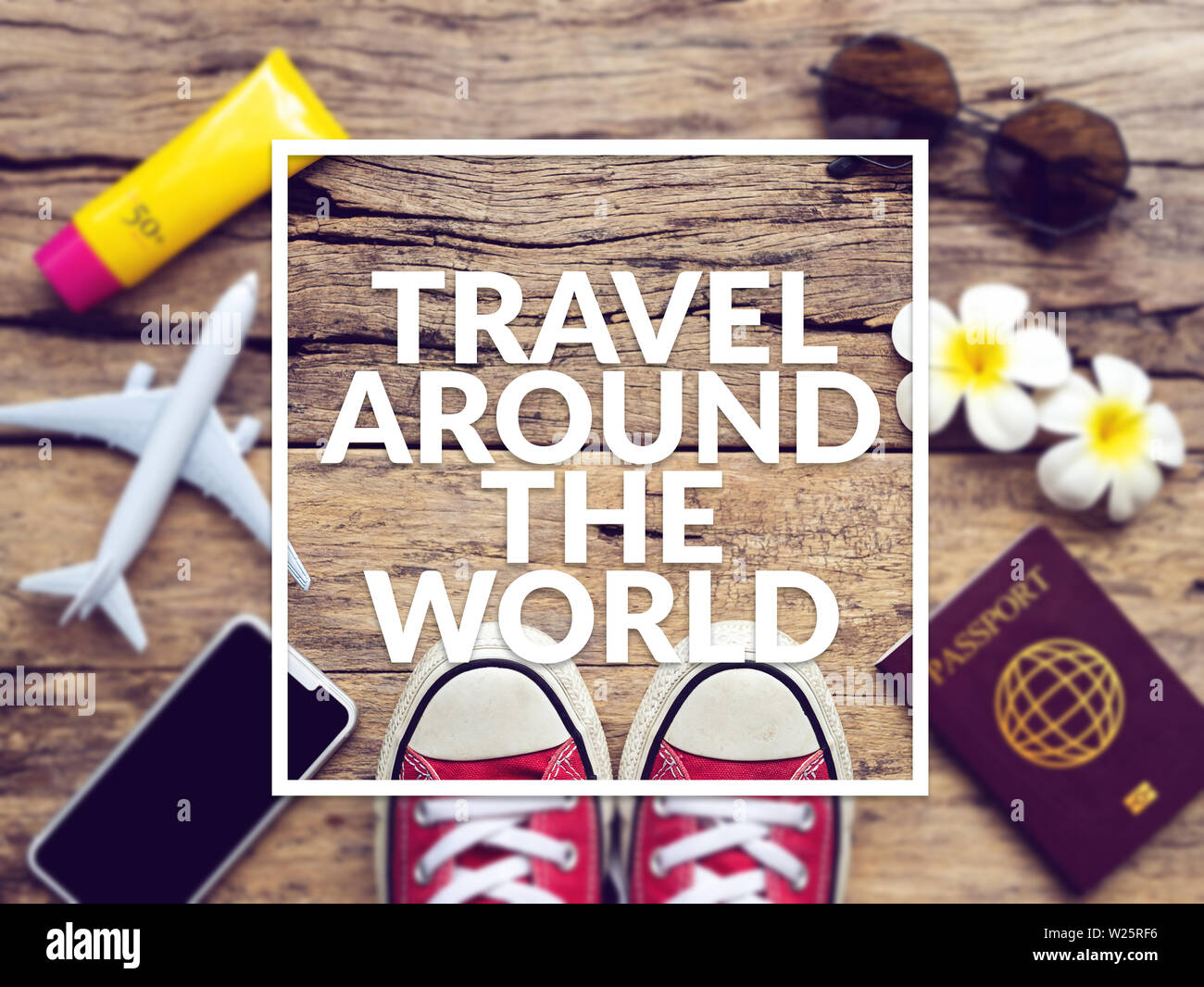 flat lay of passport , mobile , plane model , red sneakers and traveler's accessories items on wooden background with text travel around the world. Stock Photo