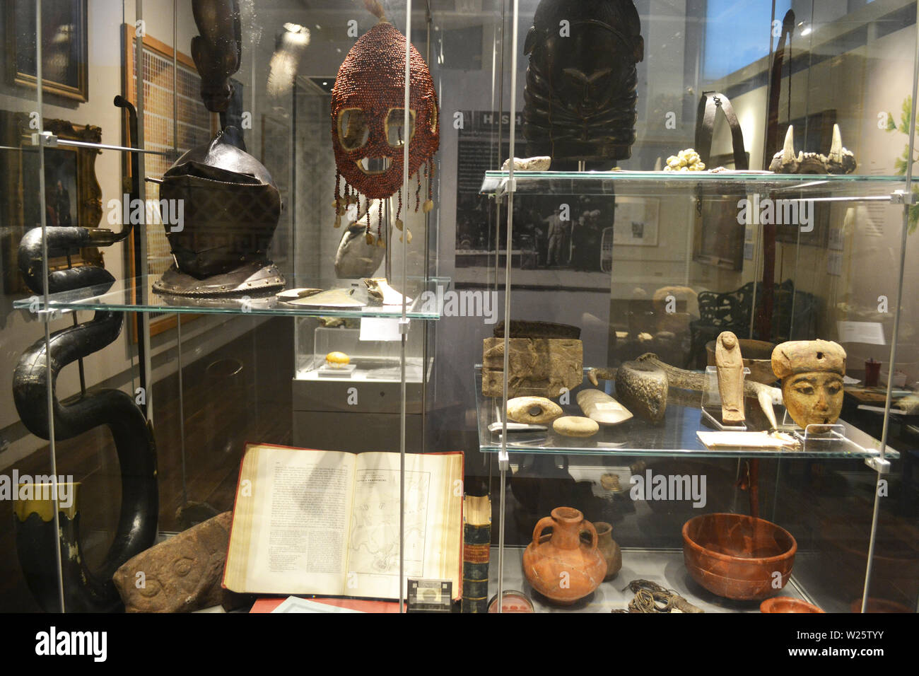 A mask, helmet, clay pot, carved figures, and other historic artifacts inside Shrewsbury Museum and Art Gallery, Shrewsbury, Shropshire, UK Stock Photo