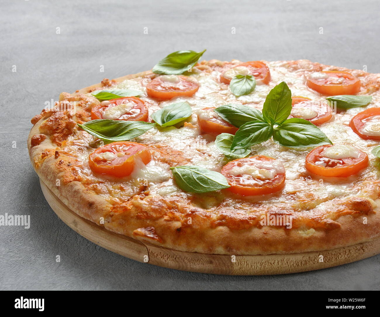 Homemade Italian Neapolitan pizza Margherita with melted mozzarella cheese and tomatoes garnished with fresh basil Stock Photo