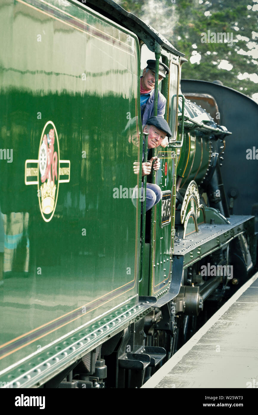A GWR vintage steam train engine pulling into Broadway heritage railway station as the engine driver and fireman look out Stock Photo