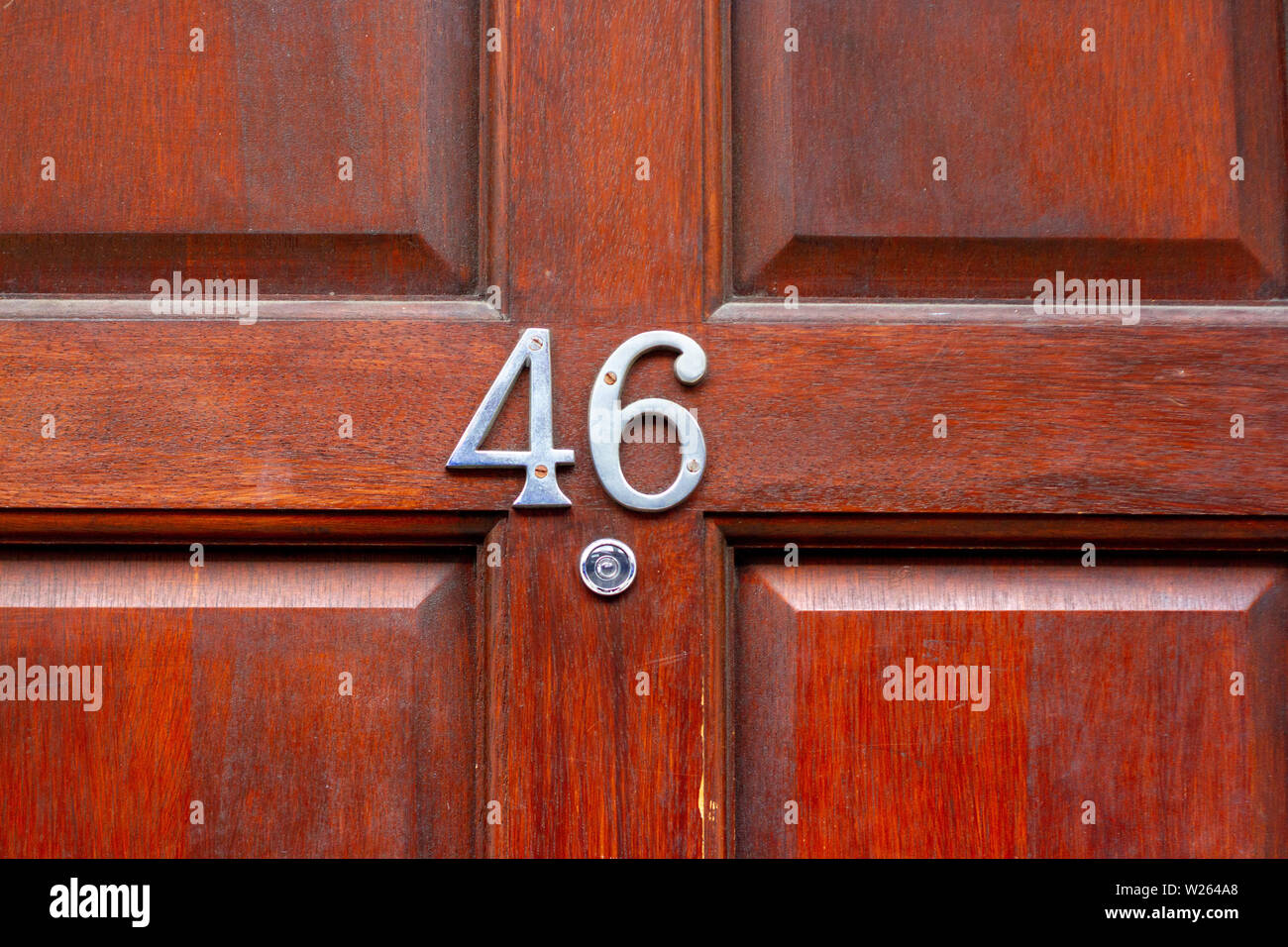 House number 46 with the forty-six in metal digits on a natural red grained wooden front door Stock Photo