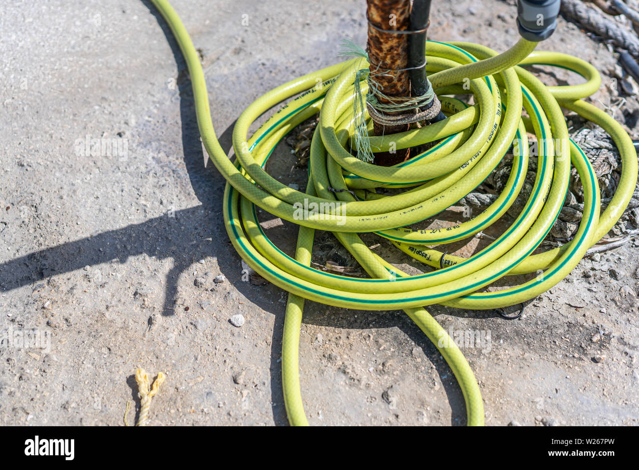 Zakynthos, Greece -  April 2019 : Yellow rubber water hose on the ground in a port in Greece Stock Photo