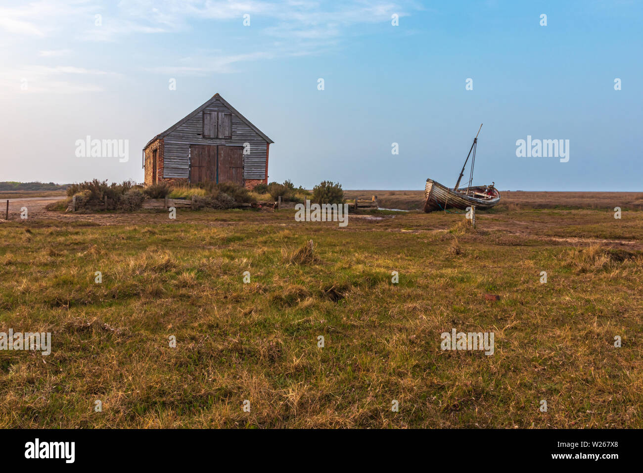 Saltmarsh coastal landscape around the old coal barn with fishing boat on its side near Thornham in North North Norfolk Stock Photo