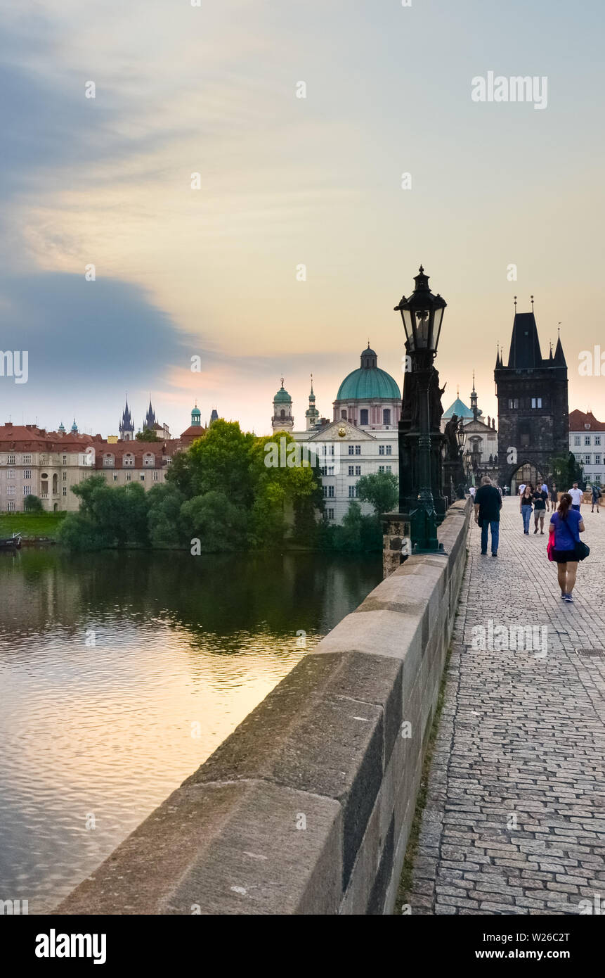 Prague, Czech Republic - June 27th 2019: People walking on historical Charles Bridge in the early morning. Sunrise light. Famous Gothic site and popular tourist spot. Bohemia, Czechia. Stock Photo