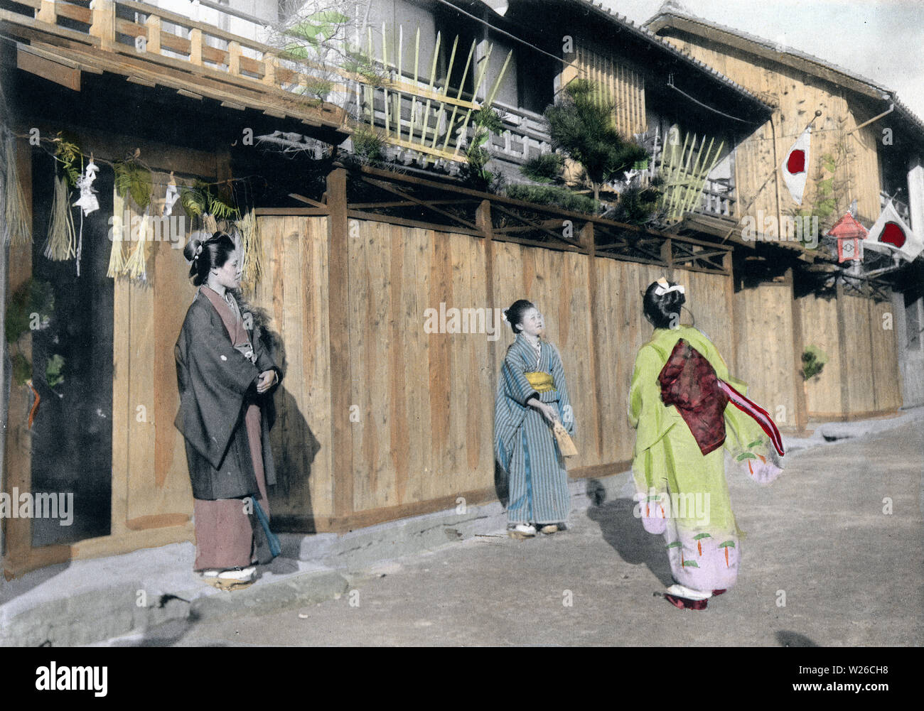 [ 1900s Japan - Japanese New Year - Playing Hanetsuki ] —   Girls play hanetsuki (battledore and shuttlecock) in front of their home, one of the traditional games played during the New Year celebrations.  This image is part of The New Year in Japan, a book published by Kobe-based photographer Kozaburo Tamamura in 1906 (Meiji 39).  20th century vintage collotype print. Stock Photo