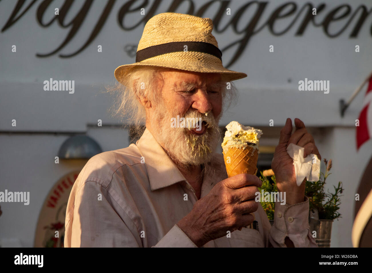 An older man enjoys an ice cream, getting ice cream in his beard and on the end of his nose Stock Photo