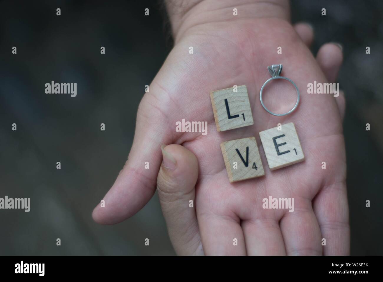 Lovers holding hands with letters and a ring spelling the word 'LOVE' Stock Photo