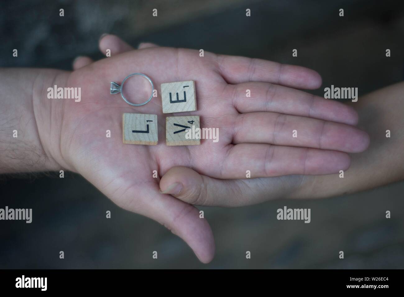 Lovers holding hands with letters and a ring spelling the word 'LOVE' Stock Photo