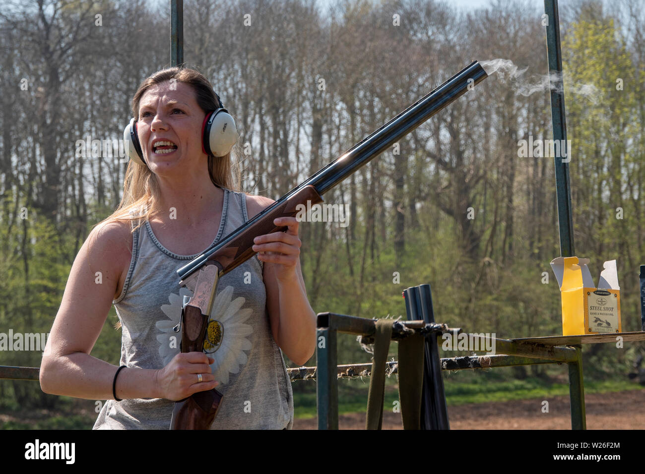 Woman standing with nsmoking open rifle at a clay pigeon shoot Stock Photo