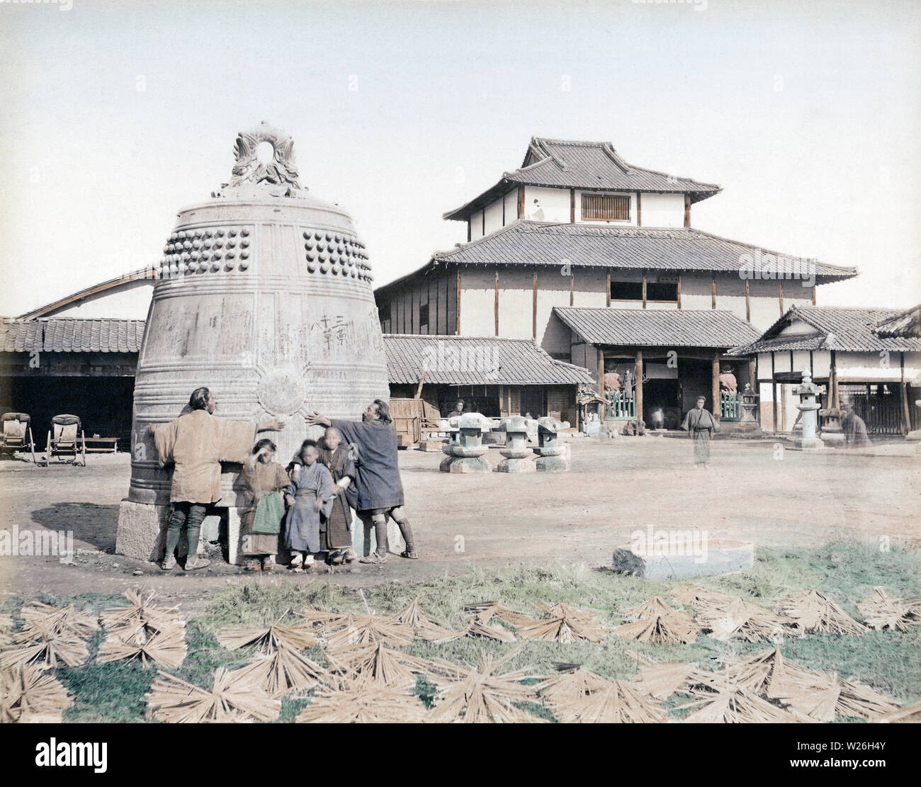 [ 1870s Japan - Chion-in Temple Bell, Kyoto ] —   Two men are stretching their arms around the bronze temple bell of Chion-in temple in Kyoto. Three children stand between them. Frames for sensu fans are drying in the foreground. In the background is Chion-in's Buddha Hall. It burnt down in 1973 (Showa 48).  The bell was cast in the early 17th century and was 4.5 meters high.  19th century vintage albumen photograph. Stock Photo