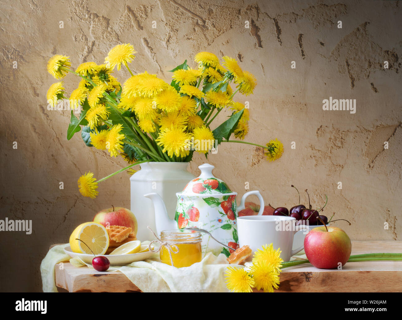 Still life with dandelions, kettle, fruit and honey on wooden table on old cracked background. Stock Photo