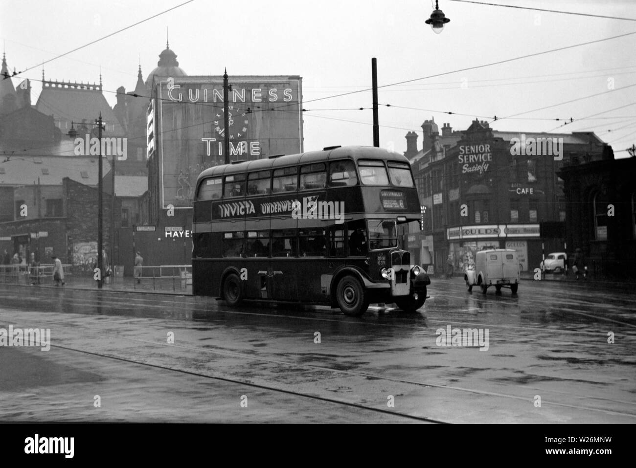 A rainy day near the Corn Exchange in Leeds city centre. The image shows a Roe Bodied AEC Regent III double decker bus on route to Cottingley. The vehicle would have been new in 1950. Note the old Guinness clock advertisement in the background. Stock Photo