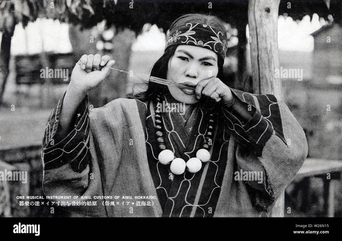 [ 1920s Japan - Ainu Woman ] —   An Ainu woman playing the Mukkuri (ムックリ, a Jew’s harp). The Mukkuri is a traditional Ainu musical instrument played by women. It is made of carefully cut bamboo with two strings.  20th century vintage postcard. Stock Photo