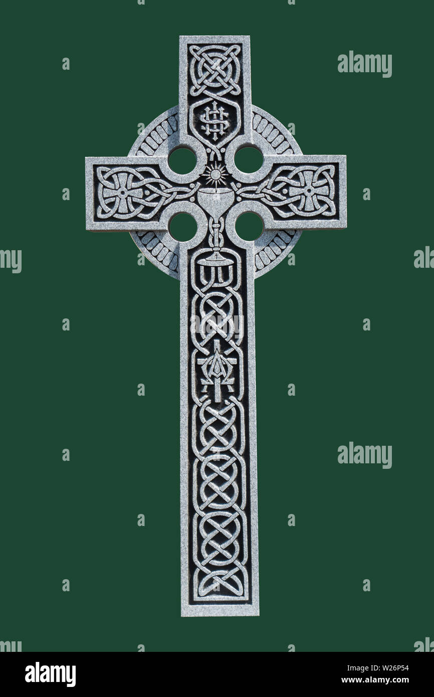 An ornate granite Celtic cross from the grave of a Roman Catholic priest, showing the Celtic knot pattern, a communion chalice, and the IHS symbol Stock Photo