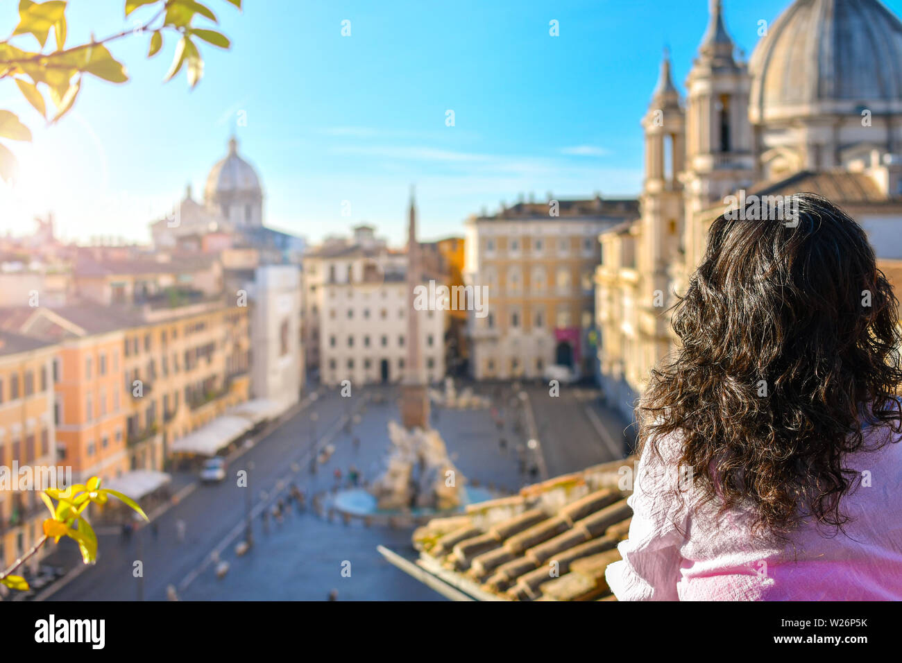 A young woman stands on a rooftop terrace of a luxury hotel overlooking Piazza Navona on a sunny summer morning in Rome, Italy. Stock Photo