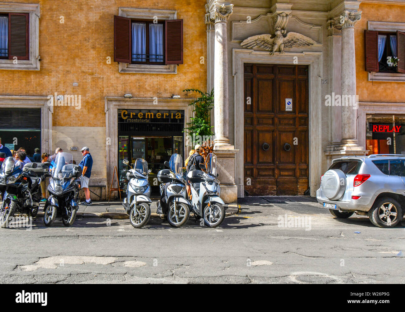 Motorcycles parked in a line outside a gelateria cremeria or ice cream shop as tourists pass by in the historic center of Rome, Italy Stock Photo