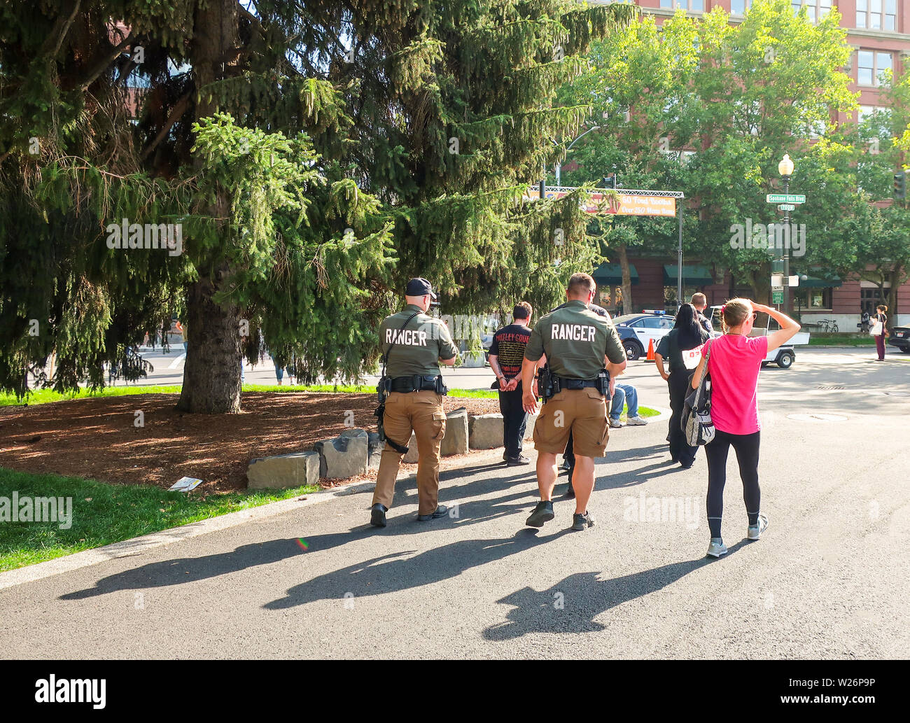 Local police and ranger officers escort a handcuffed suspect through Riverfront Park in the downtown area of Spokane, Washington. Stock Photo